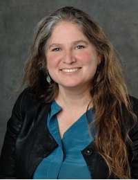 woman in blue shirt and black blazer smiling into the camera
