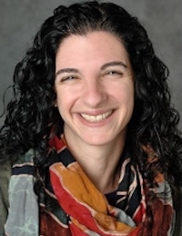 woman with dark hair wearing patterned scarf and smiling into the camera
