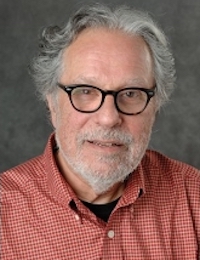 man in salmon colored shirt wearing dark framed glasses looking into the camera